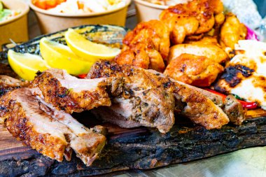 Ahşap bir tahtanın üzerinde sunulan ağız sulandırıcı bir et seçimi lezzetli pirzola, baharatlı tavuk ve taze limon dilimleri içeriyor. Renkli kenarlar iştah açıcı sunumu tamamlar.
