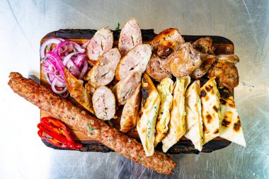 Canlı bir tabakta kebap ve baharatlı tavuk da dahil olmak üzere çeşitli ızgara etler, yanında taze soğan dilimleri ve taze soğan dilimleri yer alıyor..