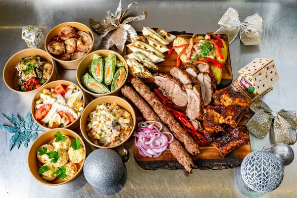 Çeşitli yemeklerden oluşan şenlikli bir düzenleme ızgara et, salata ve aperatifleri içeriyor. Hepsi de ahşap bir tabakta güzelce sunuluyor..