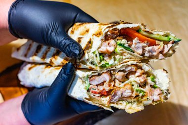 Siyah eldivenli bir şef çıtır sebze ve sosla dolu ızgara tavuk dürümü sunar. Pakette canlı malzemeler sergileniyor. Mutfak becerileri vurgulanıyor..