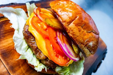Ağız sulandıran bir çizburger taze domates, turşu, soğan ve kıtır marulla dolu ahşap bir tabakta oturur. Sıcak, kızarmış çörekler sulu bir köfte ve erimiş peyniri kaplar..