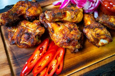 Lezzetli ızgara tavuk kanatları ahşap bir tabakta düzenlenir. Onlara canlı kırmızı biber ve soğan dilimleri ile birlikte, daldırmak için küçük bir kase sos eşlik eder. Yaz yemeği için mükemmel..