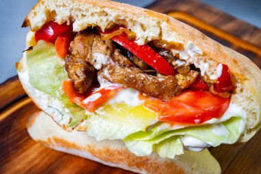 Yumuşak ızgara et, renkli biber, gevrek marul ve taze taze domateslerle dolu taze pişmiş ekmeğin üzerine serpiştirilmiş kremalı sosun tadını çıkarın..