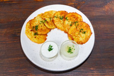 Bir tabak taze otlarla süslenmiş çıtır altın sarısı patates börekleri içerir. Yemeklere iki küçük kase kremalı sos eşlik ederek lezzetli bir lezzet deneyimi yaratıyor..