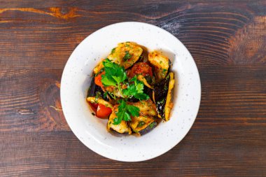 Kızarmış sebzeler, parlak vişneli domatesler ve ahşap bir masada servis edilen bir garnitür taze otlar..