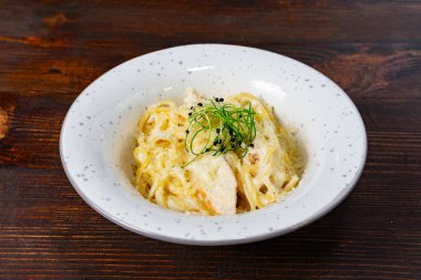 Narin otlarla kaplı bir kase kremalı makarna ahşap bir masada oturur. Tabakta zengin bir doku ve hoş bir aroma var. Sıcak bir yemek deneyimi için mükemmel..