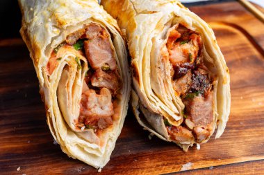 İki doyurucu paket taze et, taze sebze ve canlı soslarla doludur. Paketler altın kahverengidir ve ahşap bir tahtanın üzerinde servis edilir. Lezzetli bir yemek için mükemmeldir..