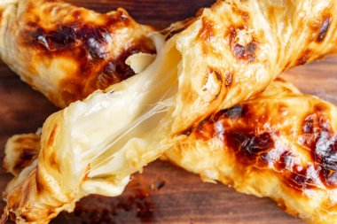 Erimiş peynirle dolu altın-kahverengi hamur işleri ahşap bir tahtanın üzerinde oturur. Yumuşak dokuları ve yapış yapış iç organları herkesi lezzetli bir ısırık almaya davet ediyor..