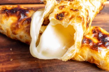 Taze pişmiş hamur işi içerideki yapışkan peyniri ortaya çıkarıyor, zengin bir altın hamuru sergiliyor. Bu iştah açıcı yemek günün herhangi bir saatinde aperatif veya aperatif için mükemmeldir..