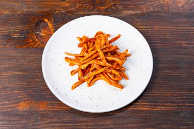 Keskin domuz kulakları, baharatlı bir baharatla kaplanmış beyaz bir tabakta ustalıkla düzenlenir. Çanak, dokulu ahşap yüzeye karşı canlı turuncu bir renk sergiliyor..