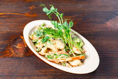 Ahşap bir masada nefis bir taze sebze salatası canlı yeşil bezelyeler, brokoli ve havuçlar içerir. Tabak mikroyeşilliklerle süslenerek cazibesini ve tadını arttırıyor..