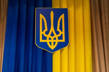 Ukrayna arması mavi ve sarı kumaşlara karşı belirgin bir şekilde gösterilir. Bu ayar, resmi bir olay veya tören sırasında ulusal gururu vurguluyor.