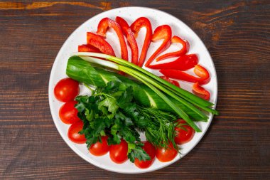 Canlı kırmızı çan biberleri, kiraz domatesleri, yeşil soğanlar ve taze otlar besleyici bir yemek için renkli malzemeler içeren bir tabakta güzelce düzenlenmiştir..