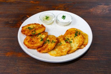 Çıtır patatesli krepler taze otlarla kaplanır ve iki küçük kase kremalı sosla servis edilir. Köy ahşap bir masada eğleniyor, lezzetli bir atıştırmalık için mükemmel..