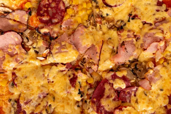 Lezzetli bir pizza ahşap bir masanın üzerinde duruyor, içinde bir tabaka erimiş peynirin altında jambon, salam, mantar ve tatlı mısır var. Sıradan bir yemek için mükemmel..