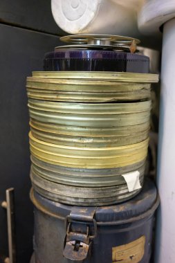 Eski film makaralarının bir koleksiyonu depodaki bir konteynıra güzelce istiflenir. Makaraların boyutları ve renkleri farklıdır, bu da sinematik bir korunma geçmişine işaret eder..