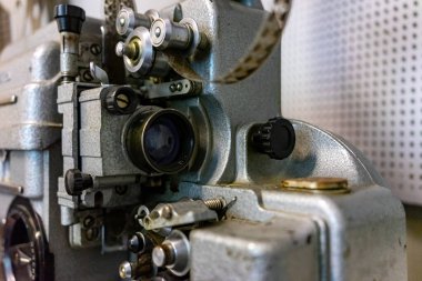 Eski bir film projektörünün yakın plan görüntüsü karmaşık mekanik bileşenlerini ortaya çıkarır. Metal parçaları yumuşak ışık altında parıldıyor, klasik film yapma teknolojisinin bir dönemini vurguluyor..
