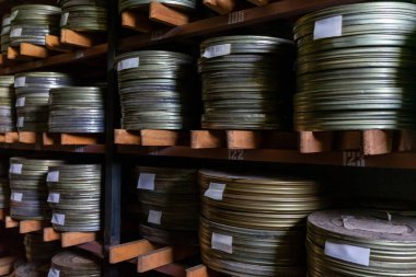 Tozlu film makaraları arşiv odasındaki ahşap raflarda düzenli olarak düzenlenir. Eski makaralar, bazıları metal kutularda, tarihi sinema hazineleri barındırıyor gibi görünüyor..