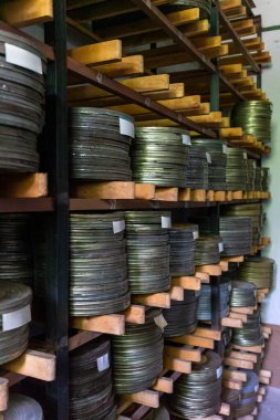 Eski bir arşiv odasındaki ahşap raflarda düzgünce düzenlenmiş sayısız film makarası var. Loş ışıklandırılmış uzay, sinema korunmasının tarihini gözler önüne seriyor..