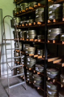 Eski film makaraları arşiv odasındaki ahşap raflarda düzgünce düzenlenir. Yakınlarda duran metal bir merdiven makaralarla dolu raflara erişimi kolaylaştırıyor.