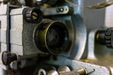 Yakın çekim, klasik bir film projektörünün karmaşık mekaniğini gözler önüne seriyor, lenslerini, düğmelerini ve desenli metal yüzeylerini vurguluyor, klasik sinema nostaljisini çağrıştırıyor..