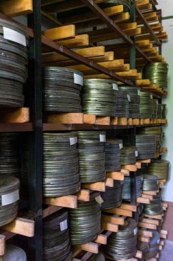 Eski bir arşiv odasındaki ahşap raflarda düzgünce düzenlenmiş sayısız film makarası var. Loş ışıklandırılmış uzay, sinema korunmasının tarihini gözler önüne seriyor..