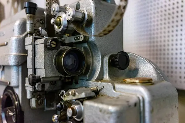 Eski bir film projektörünün yakın plan görüntüsü karmaşık mekanik bileşenlerini ortaya çıkarır. Metal parçaları yumuşak ışık altında parıldıyor, klasik film yapma teknolojisinin bir dönemini vurguluyor..