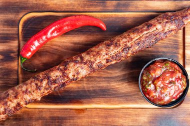 Sulu kebap ahşap bir tahtanın üzerinde duruyor, yanında da bir kase baharatlı salsa ve canlı kırmızı biber var. Günün her saatinde lezzetli bir yemek için mükemmel..