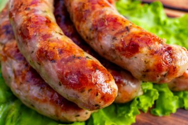 Sulu sosisler taze ızgara yapılır, altın-kahverengi bir dış görünüşü sergilenir, canlı yeşil marul üzerine yerleştirilir, servis edilmeye hazırdır. Dekor, leziz bir mutfak anını ön plana çıkarıyor..