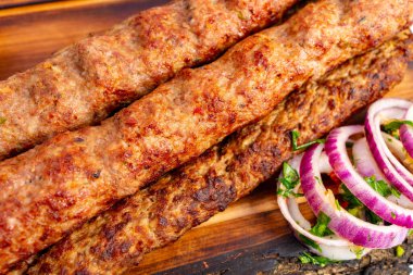 Sulu kebaplar, taze kırmızı soğanlar ve doğranmış otlarla birlikte ahşap bir tabakta mükemmel bir şekilde kızartılır..