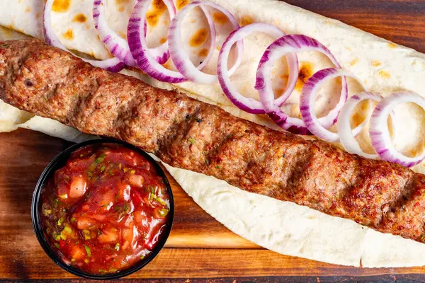 Yumuşak kebap, ince dilimlenmiş soğanla süslenmiş sıcak bir ekmeğin üzerinde oturur. Bir kase enerjik salsa yemeği tamamlar, bu da onu davetkar bir yemek seçimi yapar..
