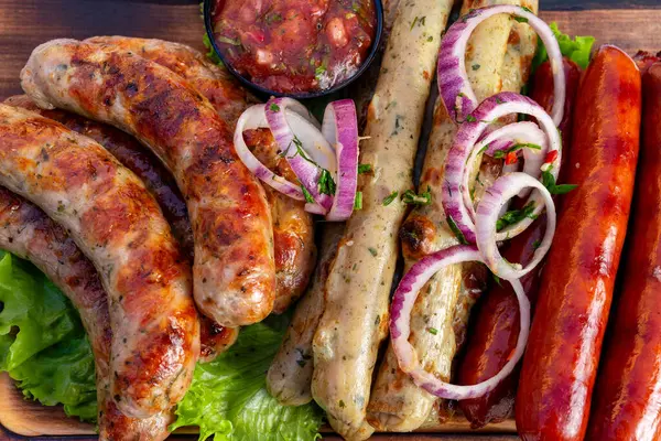 Marul yatağında ızgara sosis, dilimlenmiş soğanla süslenmiş ve yanında da bir kase salsa sosu. Yaz barbeküsünde eğlenmek için mükemmel..