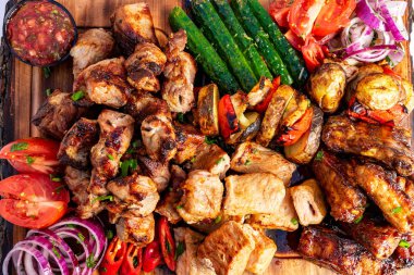 Ahşap bir tahtada rengarenk bir ızgara et ve taze sebze çeşidi sunuluyor. Sulu tavuk, biber, domates ve salatalık canlı ve iştah açıcı bir görüntü yaratır..