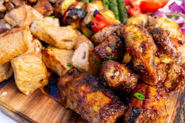 Yumuşak pirzola ve baharatlı tavuk da dahil olmak üzere çeşitli ızgara etler, canlı kızarmış sebzelerle birlikte ahşap bir tabakta güzelce düzenlenmekte ve yaz aylarında düzenlenen bir ziyafette sergilenmektedir..