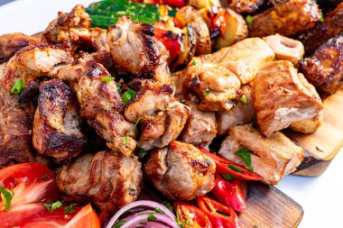 Sulu ızgara et parçaları canlı sebzelerin yanında ahşap bir tabakta düzenlenerek yaz barbeküsü için mükemmel renkli bir görüntü yaratılıyor. Dekor davetkar ve lezzet dolu..