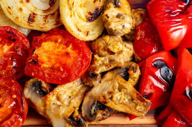 Lezzetli ızgara mantar parçaları kömürleşmiş domates, soğan ve kırmızı dolma biberlerle ahşap tabakta düzenlenir. Canlı renkler ve iştah açıcı dokular sergilenir..