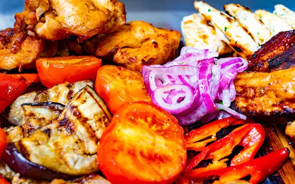 Canlı bir açık hava etkinliğinde sunulan rengarenk tavuk, domates, dolma biber ve patlıcan çeşitleri, sosyalleşmek için hazırlanmış lezzetli yemekleri gösteriyor..