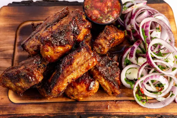 Izgara kaburgalar ahşap bir tabakta, canlı bir soğan salatası, salatalık ve salatalık ile birlikte küçük bir kase salsa sosu ile birlikte cazip bir şekilde düzenlenir..