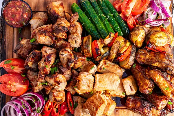 Ahşap bir tahtada rengarenk bir ızgara et ve taze sebze çeşidi sunuluyor. Sulu tavuk, biber, domates ve salatalık canlı ve iştah açıcı bir görüntü yaratır..