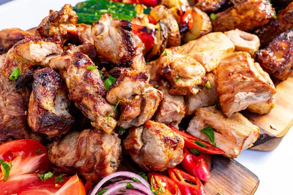 Sulu ızgara et parçaları canlı sebzelerin yanında ahşap bir tabakta düzenlenerek yaz barbeküsü için mükemmel renkli bir görüntü yaratılıyor. Dekor davetkar ve lezzet dolu..