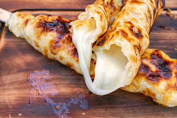 Çıtır hamurlar erimiş peynirin etrafında yuvarlanır ve rahatlatıcı bir atıştırmalık oluşturur. Bu ağız sulandırıcı ziyafet, altın-kahverengi dokusunu gösteren ahşap bir tabakta sunuluyor..