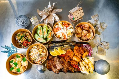 Çeşitli şenlikli yemekler metalik bir yüzeye güzelce yerleştirilmiştir. Renkli kaseler ızgara et, salata ve süslerle süslenir. Dekoratif unsurlar ve bayram süsleriyle tamamlanır..