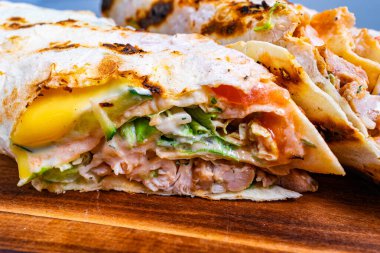 Salata ve domates gibi canlı sebzelerle dolu yeni hazırlanmış tavuk dürümünün yakın çekimi. Paket kusursuzca kızartılmış, sıcacık, kızarmış kenarları olan bir lokantada sergileniyor..