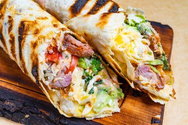 İki ızgara burrito ahşap bir tahtada sergileniyor, et, sebze ve peynir dolu canlı dolgular sergileniyor..