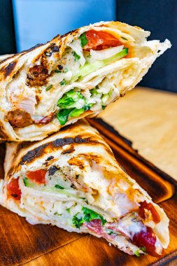 Tahta bir kesim tahtasına taze bir paket konur. Izgara tavuk, marul, domates ve sos karışımı sergilenir. Hızlı ve lezzetli bir yemek için mükemmel..