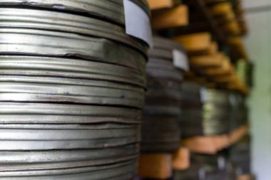 Bir deponun içindeki ahşap raflarda düzgünce istiflenmiş metal film makaraları koleksiyonu. Makara, eski bir estetiği yansıtıyor. Yıllarca kullandıkları aşınmaları ve yaşlarını gösteriyor..