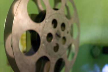 Eski bir film makarasının yakın çekim görüntüsü onun karmaşık tasarım ve detaylarını gösterir. Arka planda, sinemaseverler için nostaljik bir atmosfer olduğunu gösteren yeşil bir duvar var..