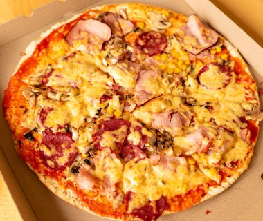Jambon, salam, mantar ve peynir de dahil olmak üzere karışık malzemelerle dolu yeni pişmiş bir pizza karton bir teslimat kutusuna konur..