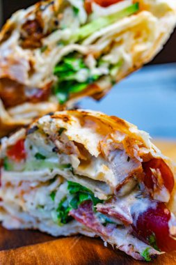 Yumuşak tavuk, taze marul ve sulu domatesleri göstermek için ağız sulandıran ızgara sargı ikiye bölünür. Tabak ahşap bir tahtada sunuluyor, canlı malzemelerini vurguluyor..