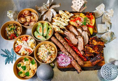 Tatil sezonu için dekore edilmiş masaya konmuş ızgara etler, mezeler ve salatalar da dahil olmak üzere çeşitli dikkatlice hazırlanmış yemekler. Şenlikli toplantılar için mükemmel.